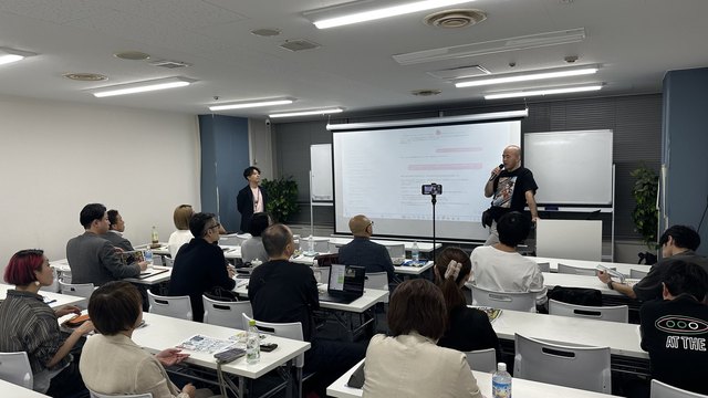講演中の会場風景。資料や画面を見ながら学ぶ参加者。